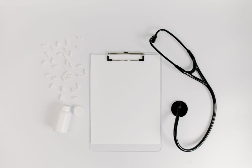 Blank clipboard with a stethoscope and white tablets on a white surface