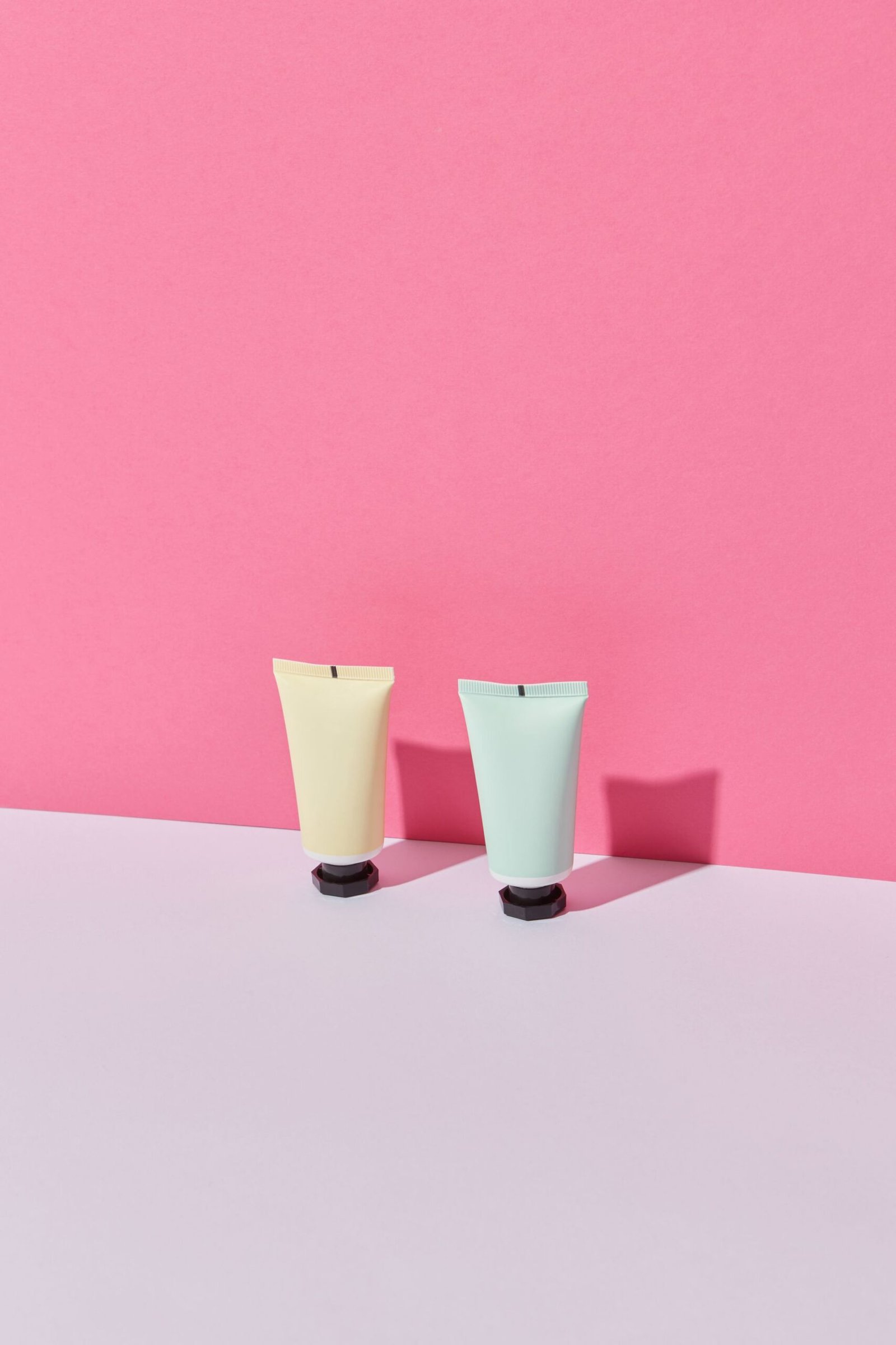 Two pastel cosmetic tubes against a pink wall