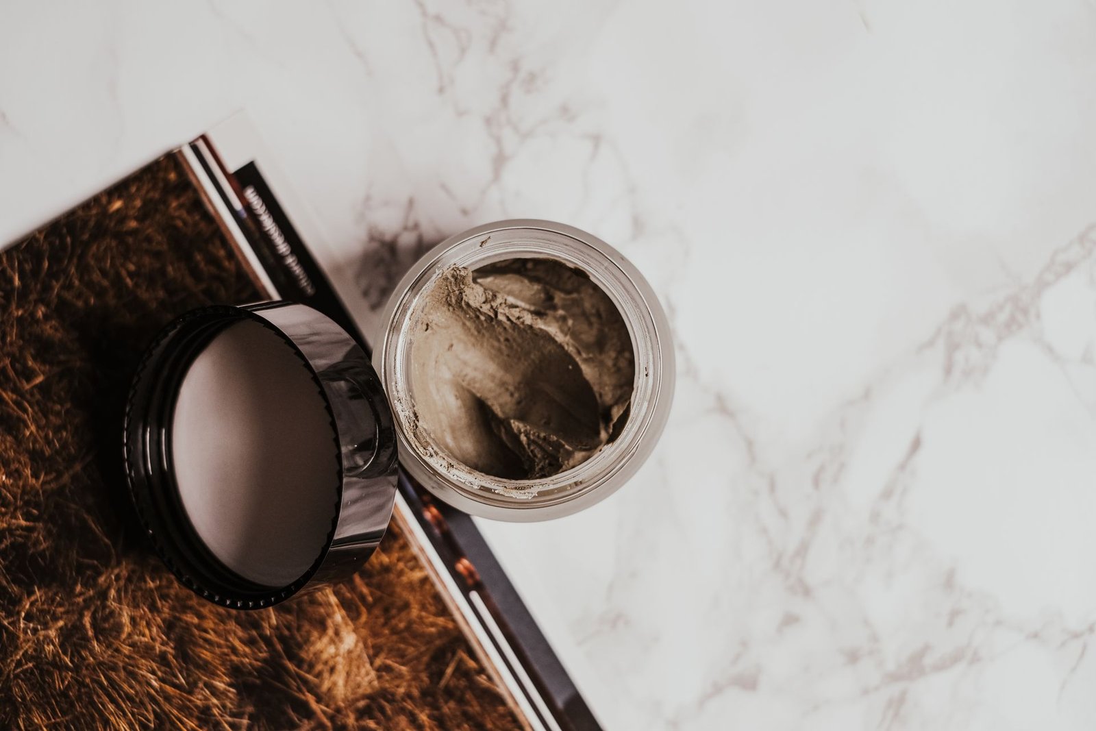 Open jar of clay mask on a marble surface