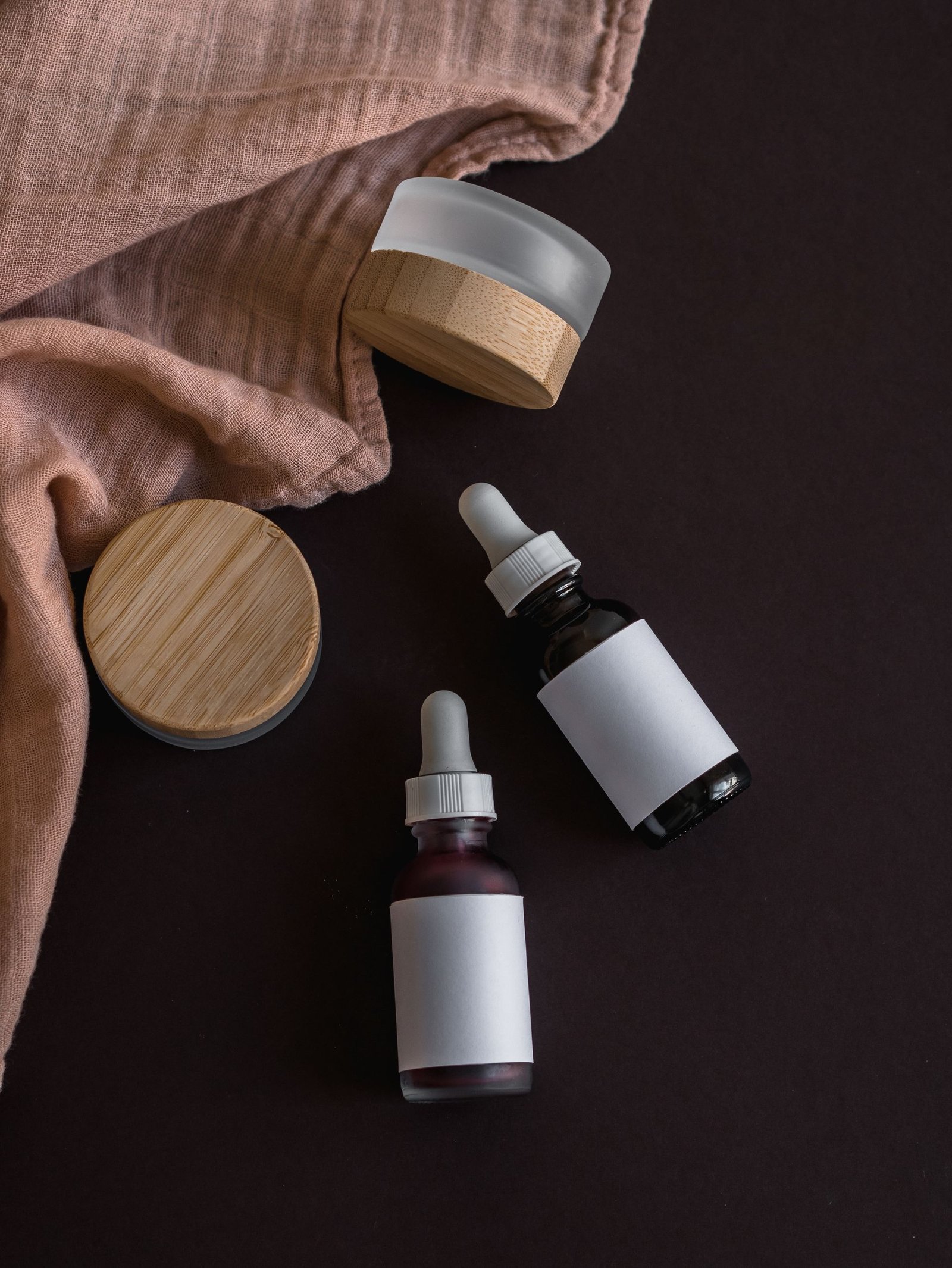 Dropper bottles and jars on a dark surface with linen