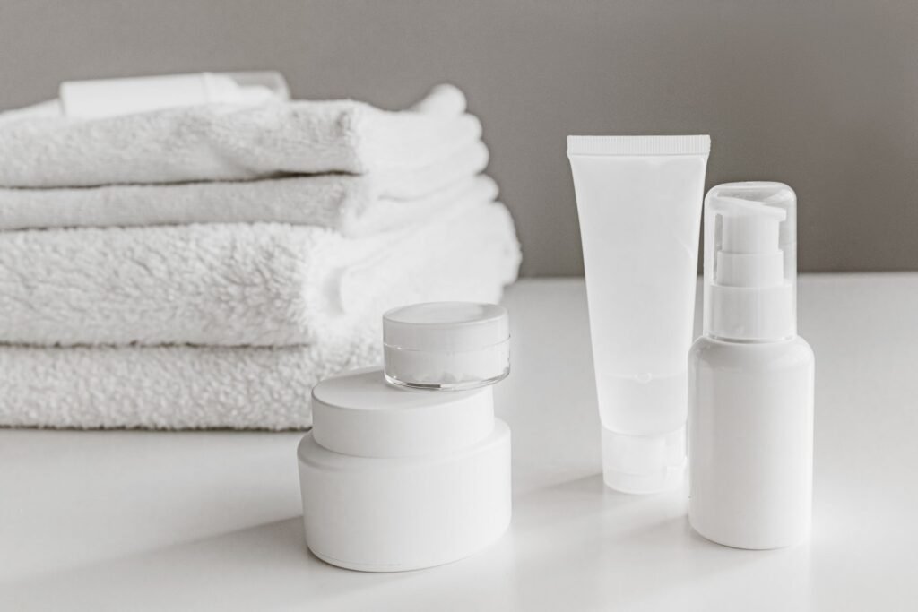 White skincare jars, tube and pump bottle beside folded towels
