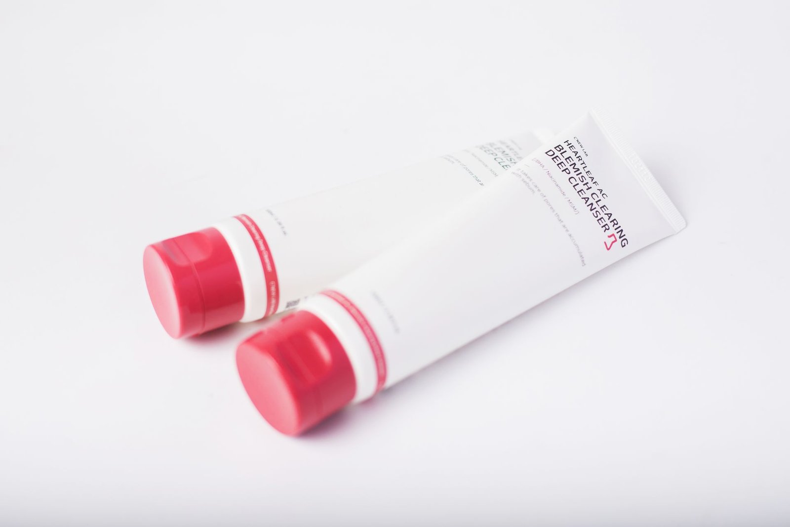 Two skincare tubes with red caps on white