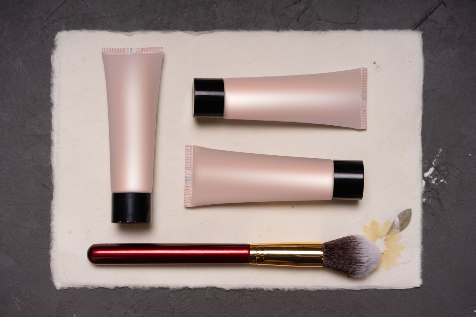 Cosmetic tubes and a makeup brush on textured paper