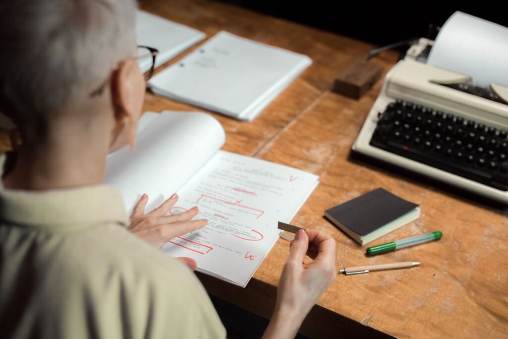 Document marked up with red pen edits beside a vintage typewriter