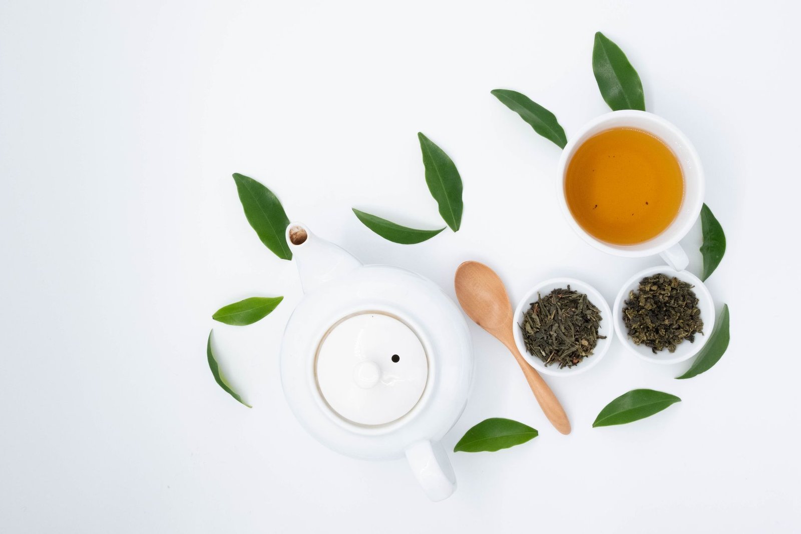 Cup of green tea with a teapot and loose tea leaves on white