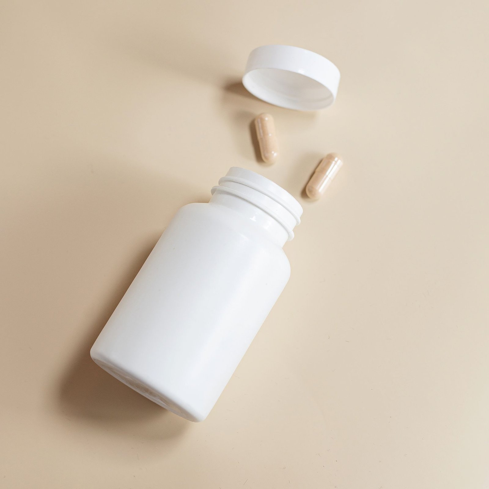 White supplement bottle with capsules on a beige background