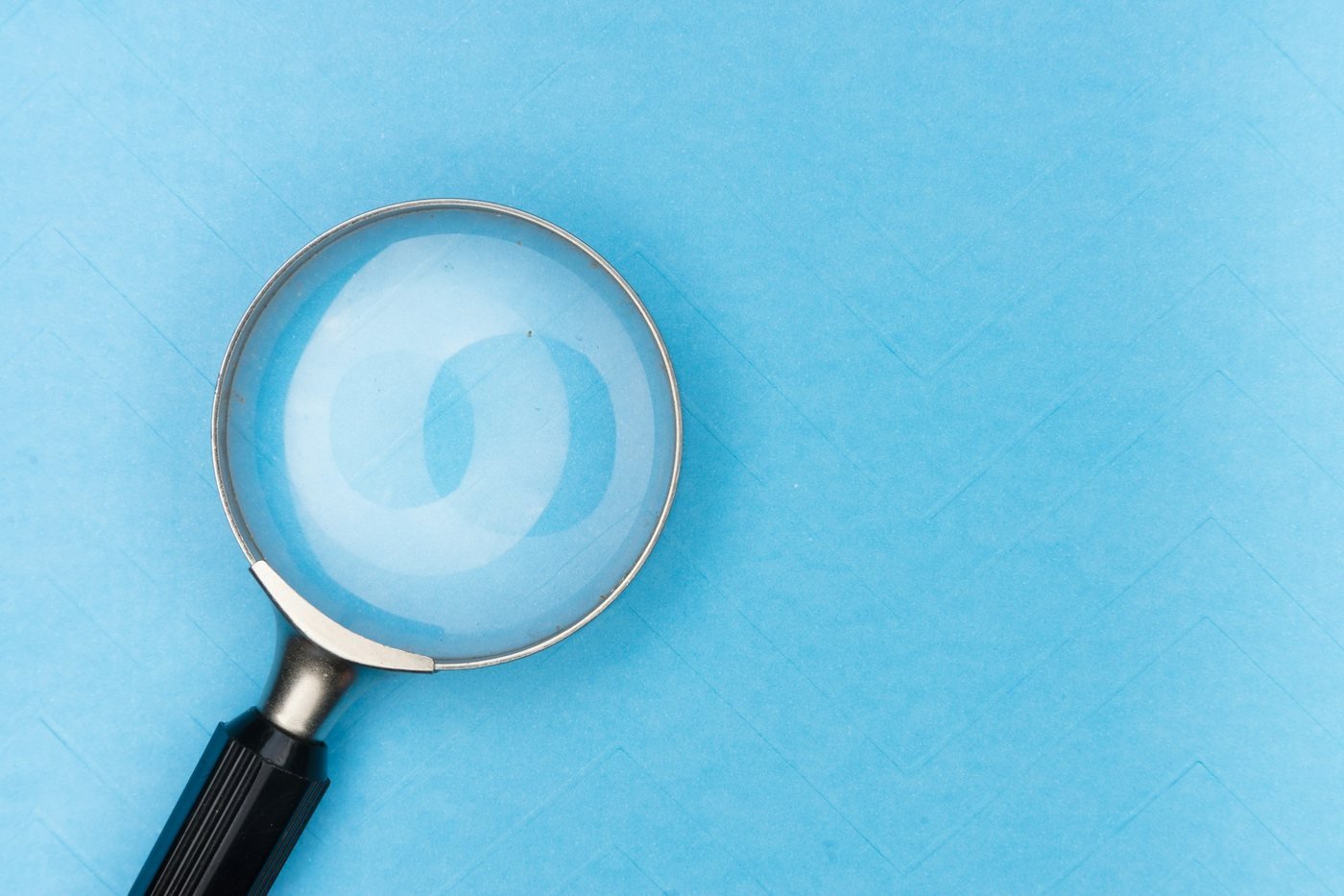 Magnifying glass on a blue surface, a tool for telling acne and rosacea apart